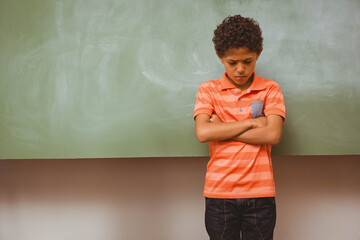 Boy standing wearing orange striped polo in classroom in front of green chalkboard, copy space