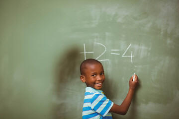 African American boy writing subtraction problem with chalk on chalkboard in classroom, copy space