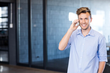 Man smiling and talking on smartphone in modern office with glass walls and polished concrete floor