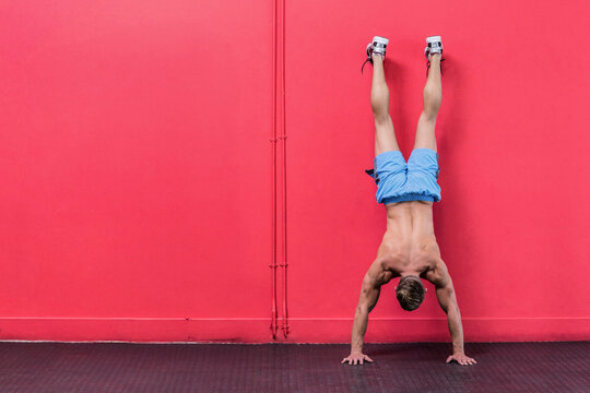 Male athlete balancing upside-down against red wall on rubber mat wearing blue shorts, copy space