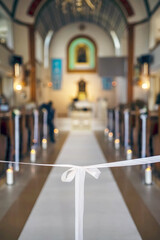 White satin bow tied to ribbon as simple wedding decoration in church interior aisle