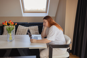 Woman sitting at desk with laptop, leaning head on hand with tired and bored expression. Concept of remote work challenges, lack of motivation, burnout, digital fatigue, procrastination, financial