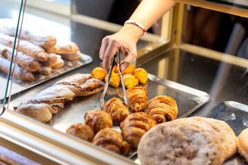 Hand selecting fresh baked croissants in bakery display