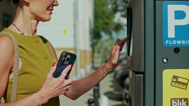 Close-up of a woman's hands as she pays for parking by putting her mobile phone to a vending machine.