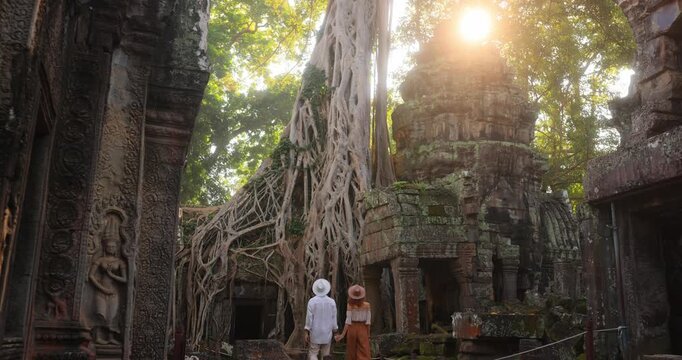 Couple Walking Through Ta Prohm Temple Ruins With Giant Tree Roots At Sunrise