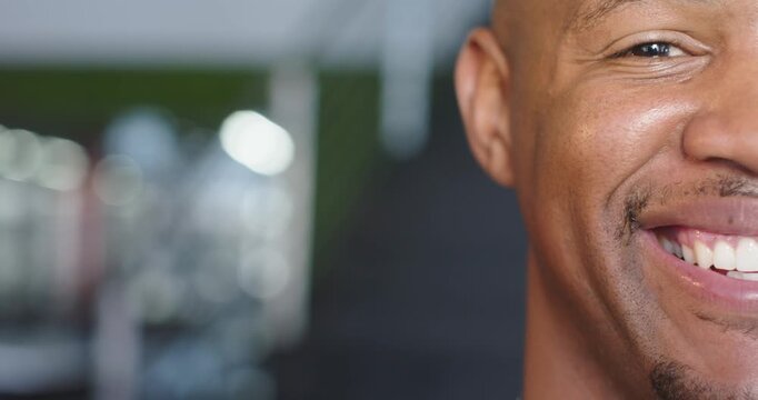 African American man smiling brightly at gym with blurred machines backdrop, copy space