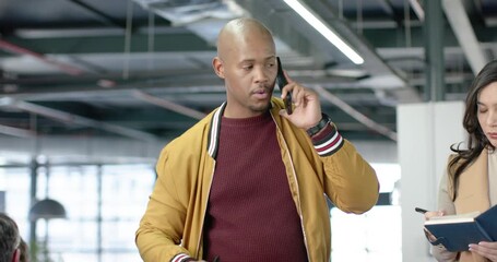 Diverse coworkers receiving smartphone call, pointing at charts and writing in notebook at office - Powered by Adobe