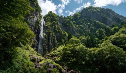 Mountain waterfall cascading down a rocky cliff face, lush green forest surrounds it