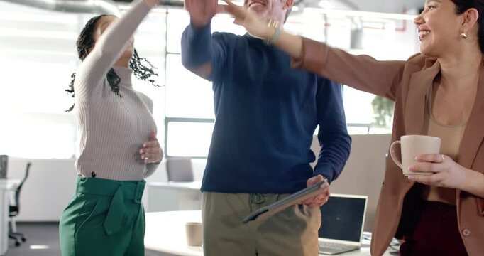 Tablet-holding man encouraging Diverse coworkers joining palms lifting arms and embracing at office