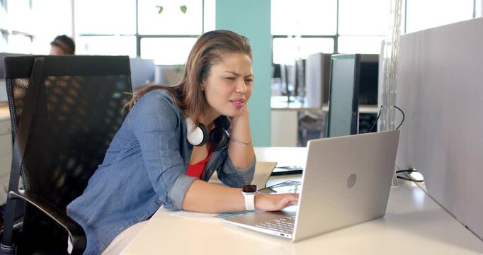Mid-adult woman studying complex graph on silver laptop at open-plan office desk clicking cursor