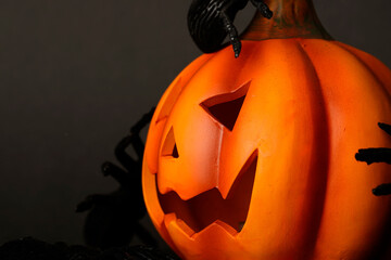 Halloween pumpkin with carved face surrounded by black spiders on dark background. Festive spooky...