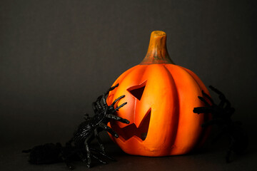 Halloween pumpkin with carved face surrounded by black spiders on dark background. Festive spooky...
