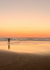 Children play on the sandy shore of Biscarosse as the sun sets, painting the sky in warm hues. The calm waves gently lap at their feet, creating a peaceful atmosphere.