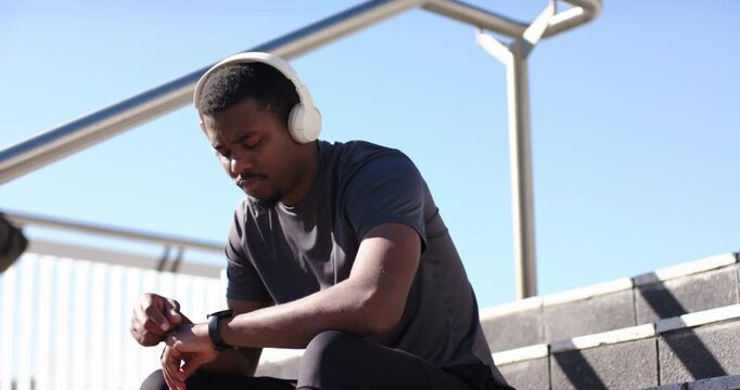 African American man tapping smartwatch to track run time during post-run break on concrete steps