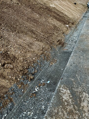 A detailed closeup image showcasing a substantial pile of dirt and gravel that is situated right next to a sturdy concrete wall, creating a contrast in textures and materials
