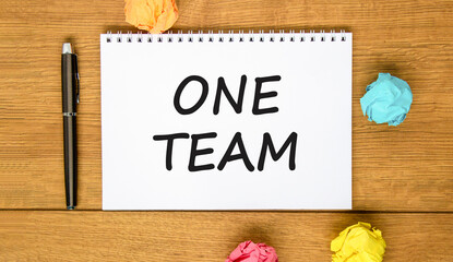 One team symbol. Concept word One team on beautiful white note. Black pen, colored paper. Beautiful wooden background. Business one team concept. Copy space.