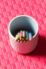 Sharpened pastel colored pencils in a ceramic cup on a colored background for drawing.