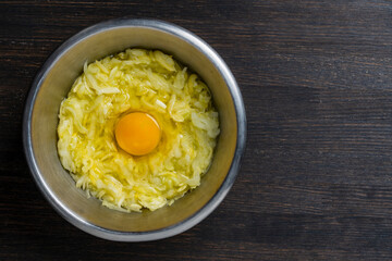 Grated zucchini with an egg in a metal bowl on a wooden table, closeup, top view, copy space. Raw materials for the preparation of vegetable waffles, pancakes. Food concept