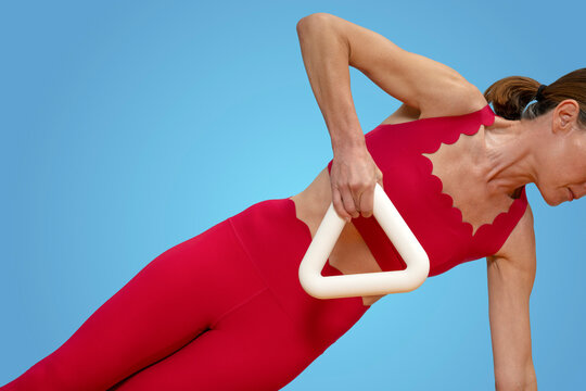 sporty woman lifting a hand weight doing a side plank exercise, red sportswear blue background