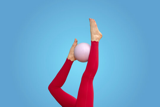 legs of a sporty woman exercising with a pilates ballet ball, red sportswear blue background