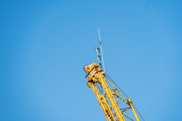 Naklejka premium Yellow and black construction crane against clear blue sky, showing multiple telescopic arm sections and mechanical attachments Perspective from below, emphasizing size and function