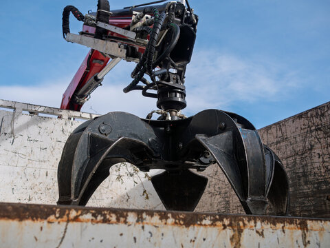 Industrial hydraulic grapple claw attachment inside truck container, showing black jaws, hoses, and rotator. Heavy-duty scrap metal handler used in recycling, salvage, demolition, and construction.