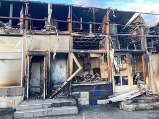 Ruined store, burnt building, charred black dark red hues, smoldering embers, twisted staircase,...