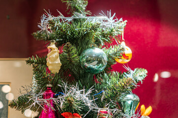 Vintage Christmas tree decorated with assorted ornaments in pastel colors against a red wall, bathed in warm, soft lighting a