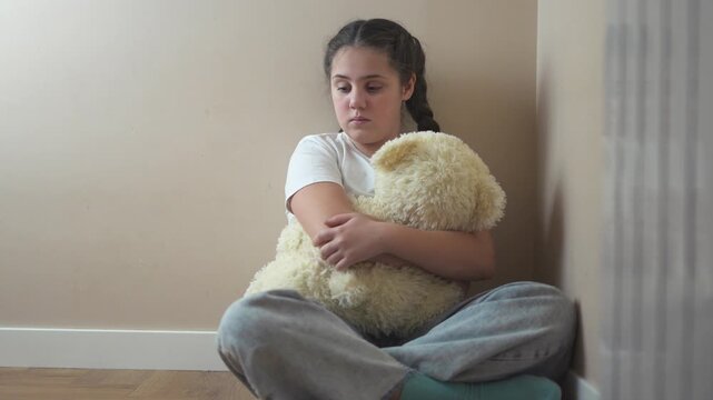 Young girl sitting on the floor with teddy bear. Teddy bear punished by sad corner. Teenage girl is traumatized by a violent attack by a teenager. A young girl lifestyle is seated on the floor with a.