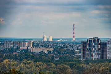 Obraz premium Aerial view of Kiev cityscape with a mix of green and yellow trees, diverse architecture including a prominent white striped water tower, power lines crisscrossing above buildings, overcast sky