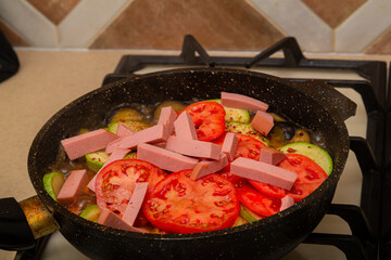 Vegetables with sausage cut into strips are fried in a frying pan