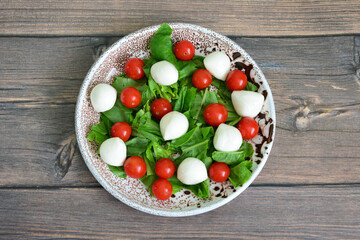 fresh salad with mozzarella, cherry tomatoes and lettuce isolated on wooden background
