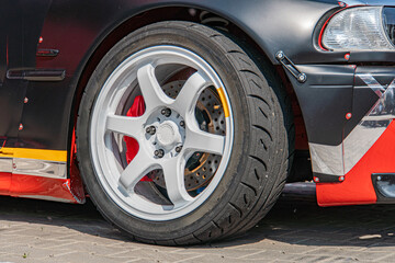 Close-up of a slightly damaged, multi-spoke wheel with chrome rims from an black-and-red repainted car a