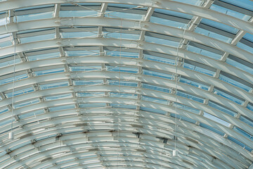 White industrial ceiling beams with geometric pattern, visible bolts, natural light filtering through openings, gray floor, expansive interior space, modern architectural photography, artistic elemen