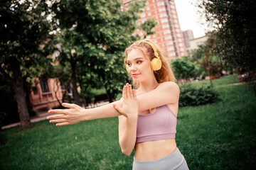 Naklejka premium Young woman stretching outdoors with headphones in vibrant city park on sunny day, exemplifying vibrant fitness and wellness