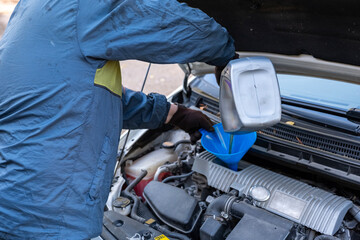 A man pours motor oil from a plastic canister into a car engine. Car servicing outdoors.