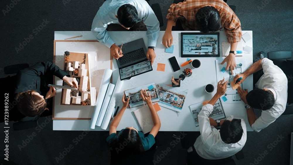 Poster top view of smart architect engineer writing at blueprint while sitting at meeting table with house 