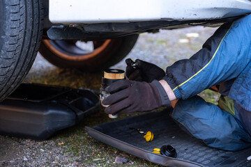 A man lies under a car, changing the oil filter in the car himself.