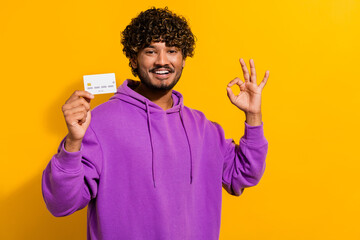 Young man in casual hoodie holding a card with cheerful expression on vibrant yellow background...