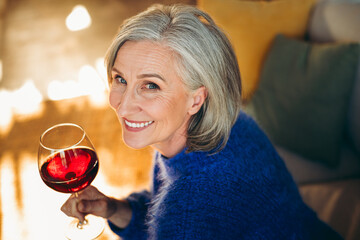 Charming senior woman enjoying wine in a cozy living room during daylight hours