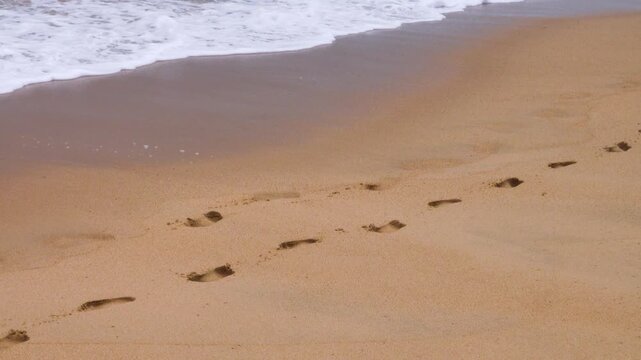 Traces of human feet, impression of a foot. Two chains of footprints along the edge of the sea and the sandy beach, the waves wash away the tracks