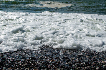 Waves crashing on rocky shoreline at midday, creating white foam and splashes
