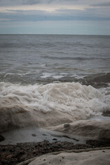 Waves crashing on rocky shore under a cloudy sky at dusk near a serene coastline