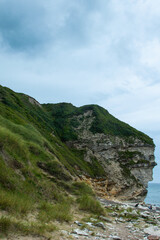 Naklejka premium Stunning coastal view at a rocky cliff with lush green hills under a cloudy sky