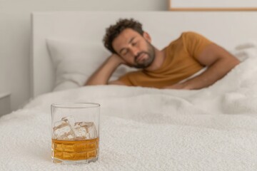 A man sleeps soundly in bed, a glass of whiskey with ice sits on the white bedding nearby