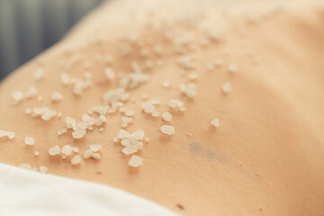 Closeup woman customer having exfoliation treatment in luxury spa salon with warmth candle light ambient. Salt scrub beauty treatment in health spa body scrub. Quiescent