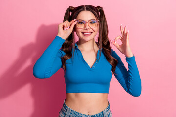 Obraz na płótnie Canvas Cheerful Young Woman in Blue Top and Glasses Making Hand Gesture Against Pink Background