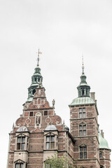 Historic architecture in Denmark features ornate towers and intricate brickwork under a cloudy sky