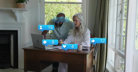 Senior woman typing on laptop causing social icons rising on charts while man annotating engagement - Powered by Adobe