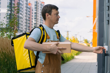 Delivery courier in uniform with a bright yellow thermal backpack pressing a doorbell while holding...